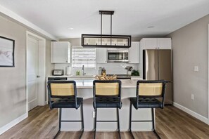 A modern kitchen with white cabinets, a central island with bar stools, and a hanging light fixture.