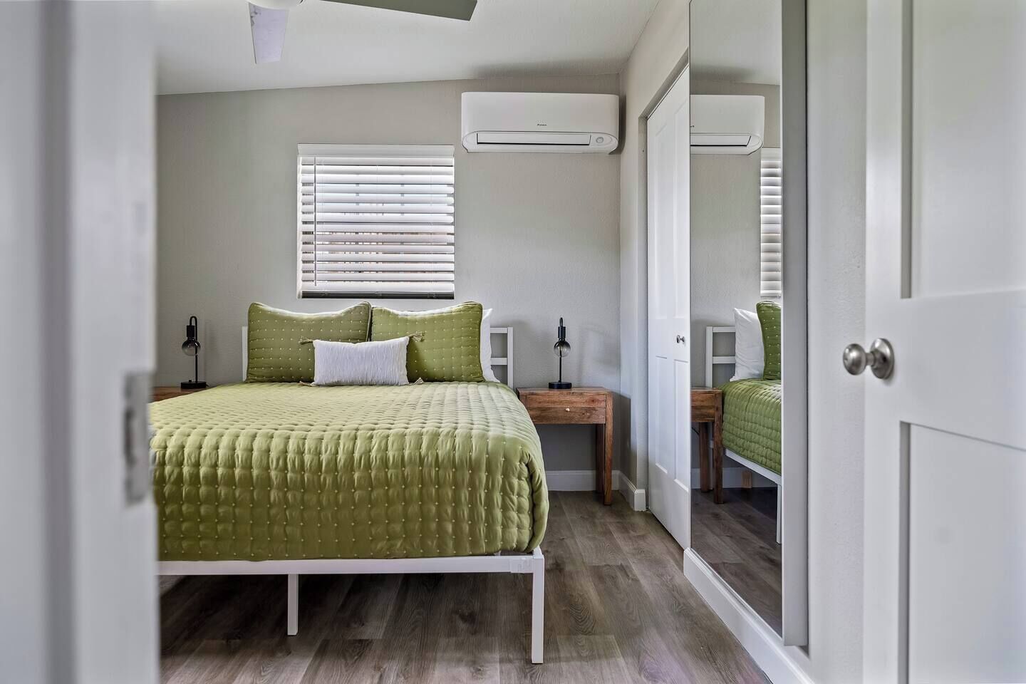 Een slaapkamer met een bed, nachtkastjes, een raam met jaloezieën, een airconditioning en een deur.