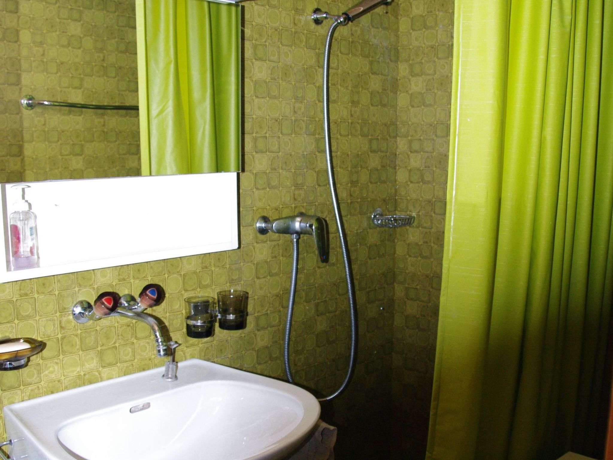 Ein Badezimmer mit einem weißen Waschbecken, einem Spiegel, einer Dusche und grünen Vorhängen.