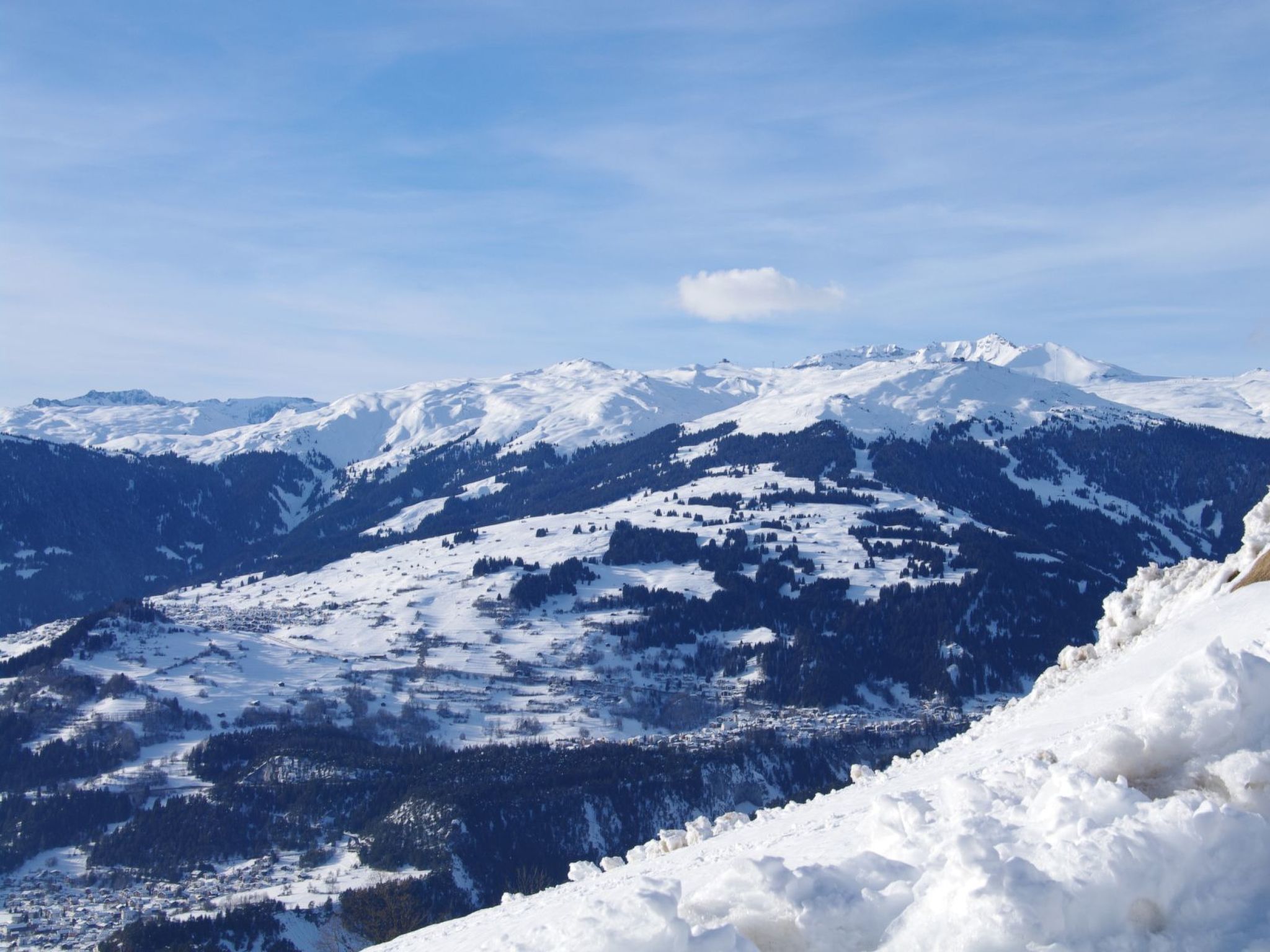 A panoramic view of a snow-covered mountain landscape with a small settlement at the base.