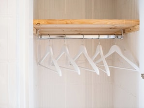 A wooden closet with a metal rod holding white hangers.