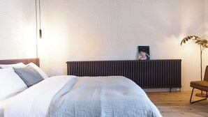 Une chambre à coucher avec un lit, un radiateur, une chaise et un tableau accroché au mur.