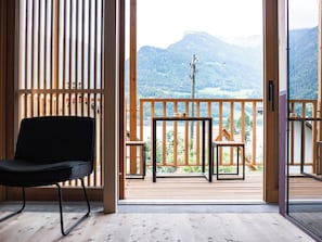 A wooden deck with a black chair and a small table, overlooking a mountainous landscape.
