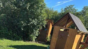 Et træbord til picnic i en græsplæne med en træbygning i baggrunden.