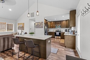 A modern kitchen with a central island, bar stools, wooden cabinets, and pendant lighting. - 14-Acre Mountain Escape - Hot Tub + Fire Pit (Nehalem)
