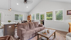A spacious living room with a brown sofa, a wooden coffee table, and a kitchen area in the background. - 14-Acre Mountain Escape - Hot Tub + Fire Pit (Nehalem)