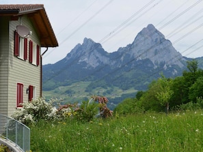 Une maison avec des volets rouges, un toit en pente et une vue sur une chaîne de montagnes.