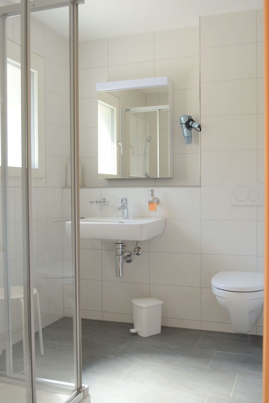 Une salle de bain avec une douche à parois de verre, un lavabo blanc avec un miroir au-dessus et des toilettes.