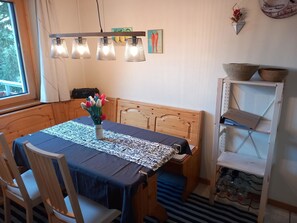 Een eetruimte met een houten tafel, stoelen, een tafelkleed met een patroon en een vaas met bloemen.