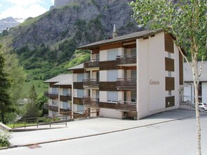 A multi-story hotel with balconies, a mountain backdrop, and a parking area. - Gstein E3 # 4-bed apartment, Bad, WC 4-bed apartment, Bad, WC by Interhome (Leukerbad)