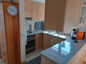 A kitchen with wooden cabinets, a built-in oven, a granite countertop, and a clock on the wall. - Gstein E3 # 4-bed apartment, Bad, WC 4-bed apartment, Bad, WC by Interhome (Leukerbad)