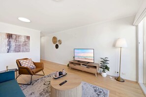 Una sala de estar moderna con televisor de pantalla plana, un sillón de cuero marrón, una mesa de centro redonda y una lámpara de pie.