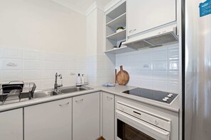 A modern kitchen with white cabinetry, a stainless steel sink, a built-in oven, and a range hood. - Spacious 2-Bedroom Retreat with Golf Course Views (Narrabundah)