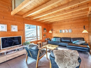 Ein gemütliches Blockhaus-Interieur mit Fernseher, Sofa und Sesseln.