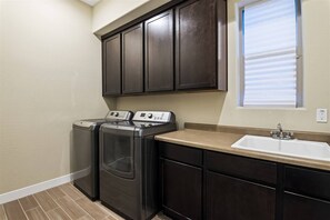 A laundry area with a washing machine and dryer, a sink, and dark wooden cabinets. - Troon: Scottsdale Condo, Views & Heated Pool (Scottsdale)