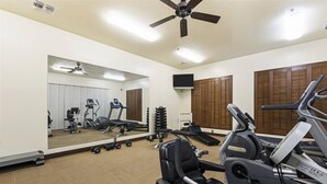 Une salle de sport équipée de matériel d’exercice, dotée d’un ventilateur de plafond et d’un grand miroir.