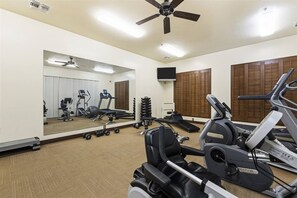 Ein Fitnessraum mit Trainingsgeräten, einem Deckenventilator und einem großen Spiegel.