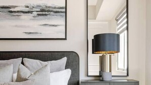 Une chambre à coucher avec un lit, des oreillers, une table de chevet avec une lampe, une armoire et un tableau abstrait encadré accroché au mur.