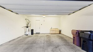 Un garage avec un sol en béton, une porte blanche, un chauffe-eau et des bacs de rangement.
