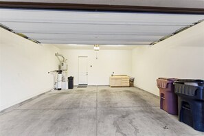 Eine Garage mit Betonboden, einer weißen Tür, einem Warmwasserspeicher und Aufbewahrungsbehältern.