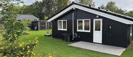 Een zwarte houten chalet met een witte deur en ramen, een gazon en een houten terras.