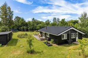A modern house with a dark exterior, a sloped roof, and a deck with outdoor furniture. - Holiday home near the water on scenic Møn (Askeby)
