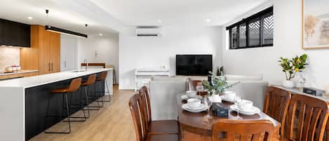 A modern kitchen with a central island, bar stools, and a dining area with wooden chairs and a table set for four.