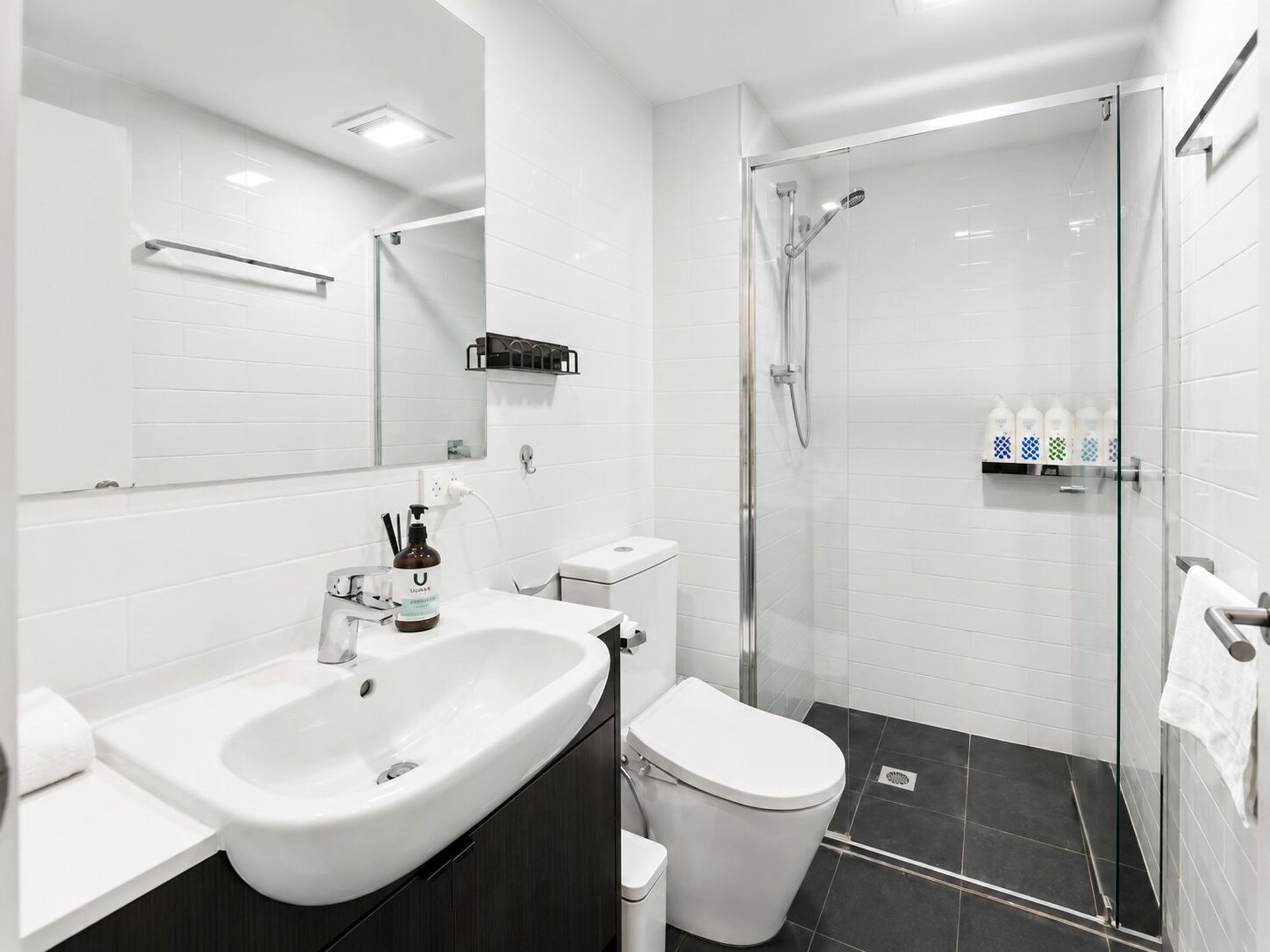 A modern bathroom with a white sink, toilet, and shower area.