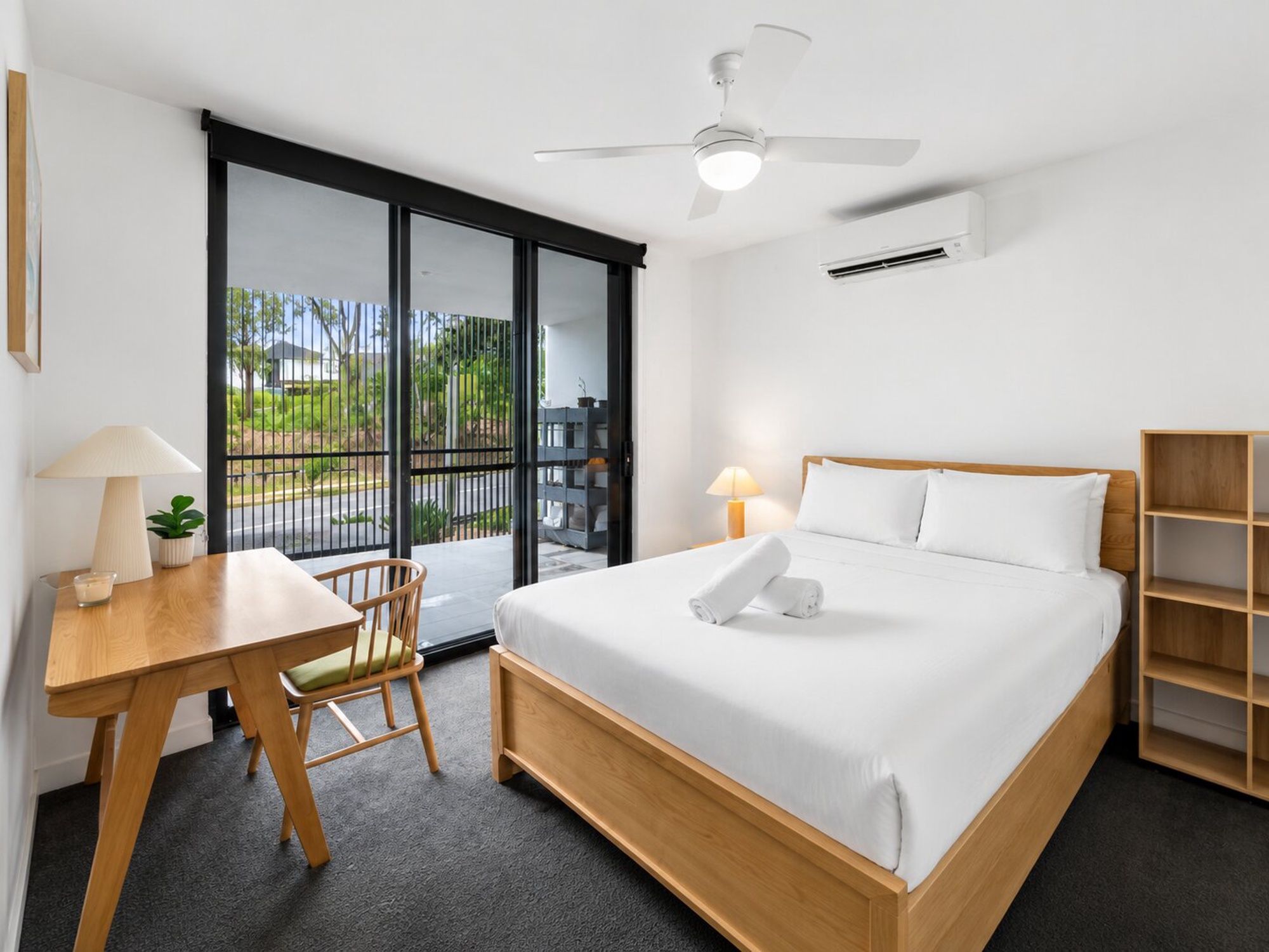 A hotel room with a bed, a desk, a chair, a ceiling fan, and a view of the outdoors.