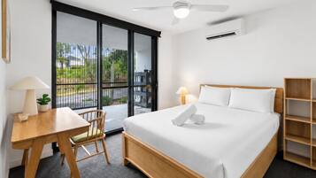 A hotel room with a bed, a desk, a chair, a ceiling fan, and a view of the outdoors.