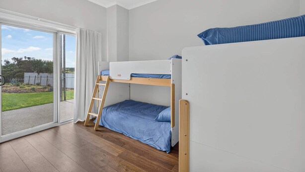 Camera con letto a castello, scala in legno, porta scorrevole in vetro che dà su un giardino e ventilatore a soffitto.