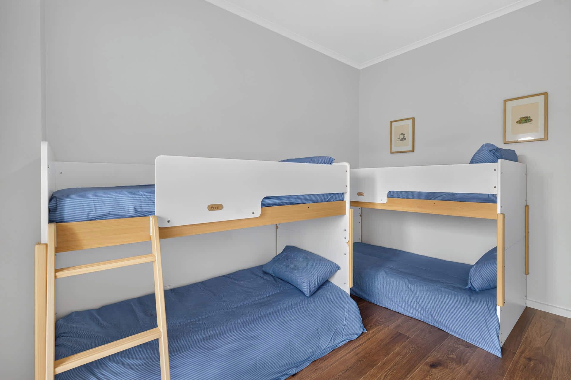 Um quarto com duas beliches, cada uma com estrutura de madeira e roupa de cama azul.