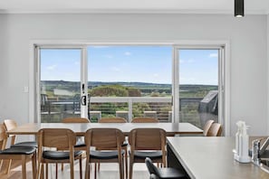 A dining area with a view of the countryside through large windows. - Beachside Family Escape 92 Newell Avenue Middleton Spacious 4-Bedroom Holiday Home Sleeps 10 one street from Middleton Beach (Middleton)