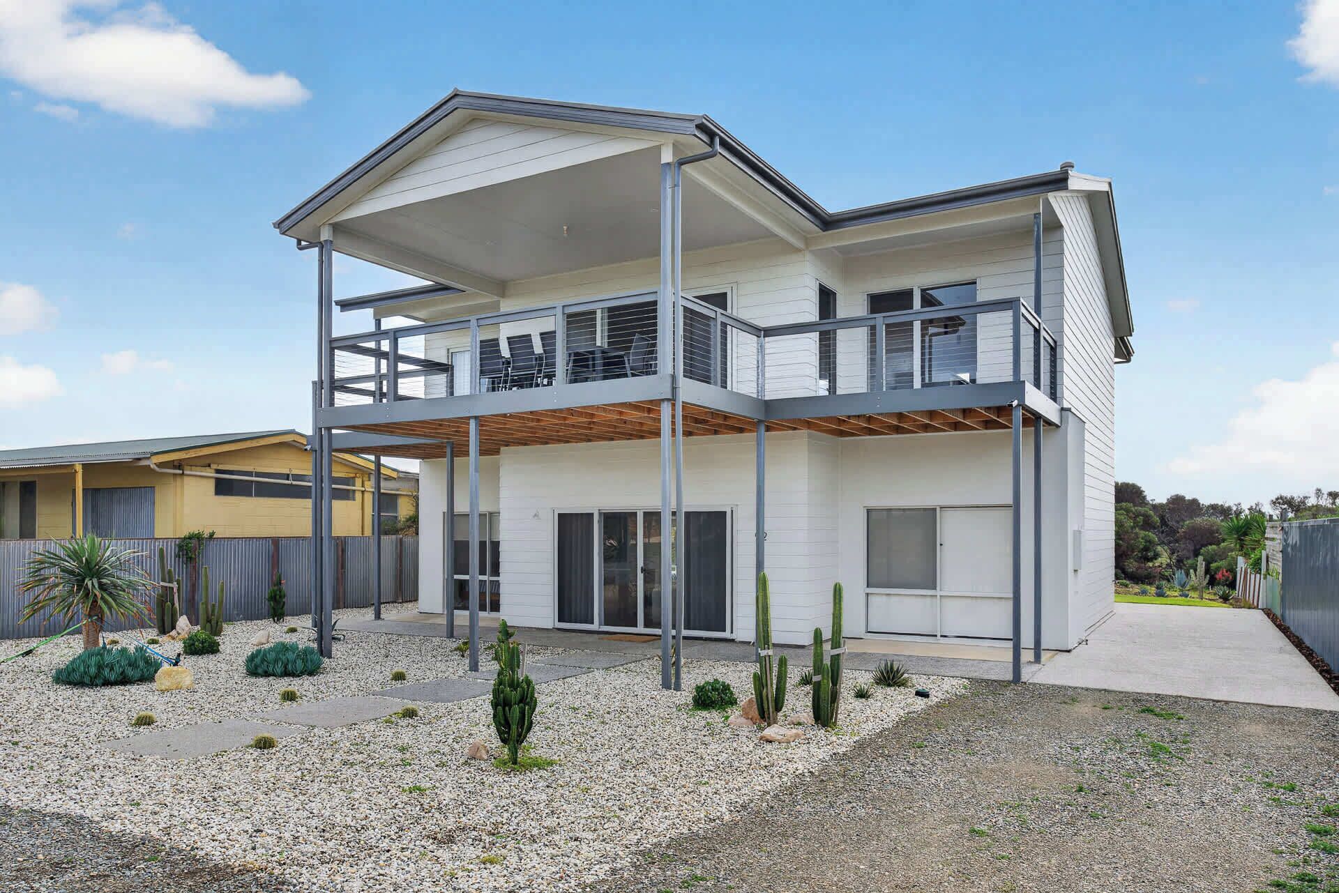 A modern two-story house with a balcony, a covered patio, and a landscaped garden with cacti.