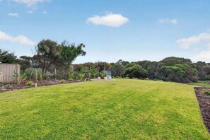 A well-maintained grassy yard with a shed and a small structure, surrounded by dense trees and shrubs. - Beachside Family Escape 92 Newell Avenue Middleton Spacious 4-Bedroom Holiday Home Sleeps 10 one street from Middleton Beach (Middleton)