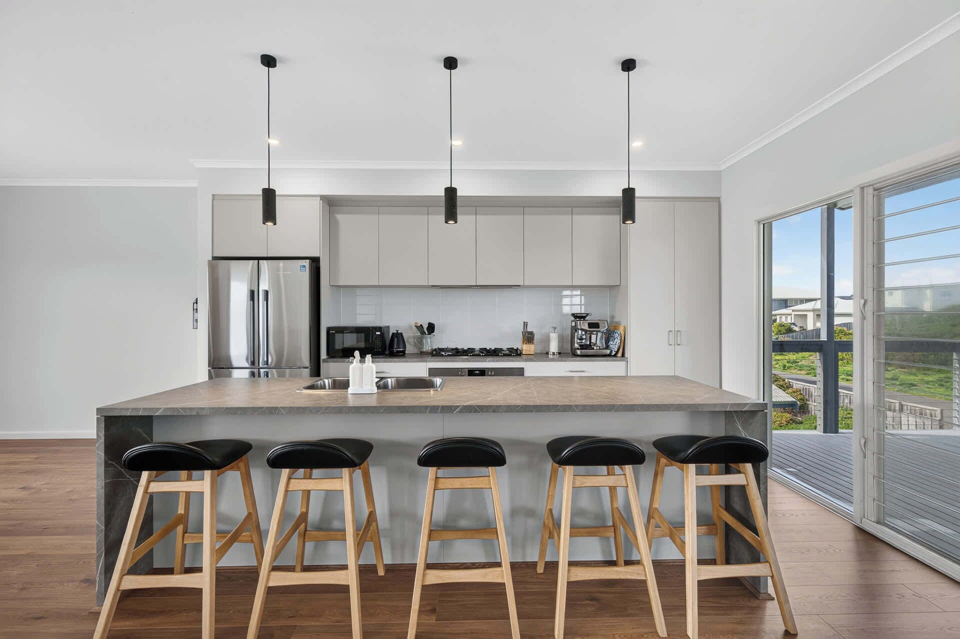 Une cuisine moderne dotée d’un îlot central, de tabourets de bar, d’appareils électroménagers en acier inoxydable et d’une grande fenêtre offrant une vue dégagée.