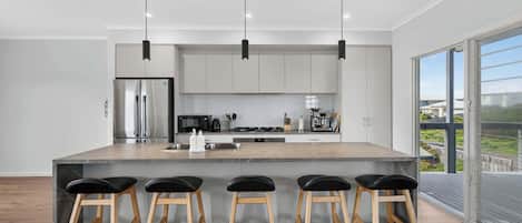 Une cuisine moderne dotée d’un îlot central, de tabourets de bar, d’appareils électroménagers en acier inoxydable et d’une grande fenêtre offrant une vue dégagée.