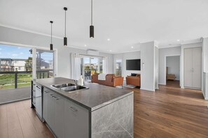A modern kitchen with a marble countertop, a built-in sink, and a dining area with a sofa and a TV. - Beachside Family Escape 92 Newell Avenue Middleton Spacious 4-Bedroom Holiday Home Sleeps 10 one street from Middleton Beach (Middleton)