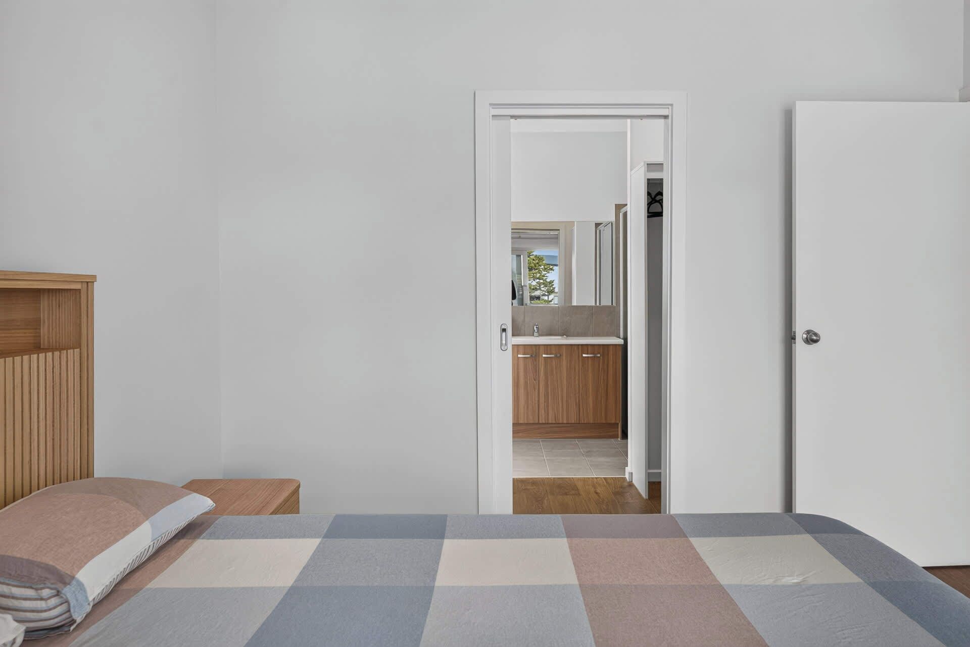 Ein Schlafzimmer mit Bett, Nachttisch, Kleiderschrank und einer Tür zu einem Badezimmer mit Spiegel und Waschbecken.