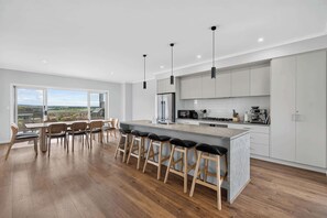 Una cocina moderna con una isla central, taburetes de bar y vistas a través de la puerta de cristal.
