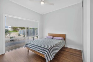 Ein Schlafzimmer mit einem Bett, einem Deckenventilator und Blick auf einen Garten durch ein großes Fenster.