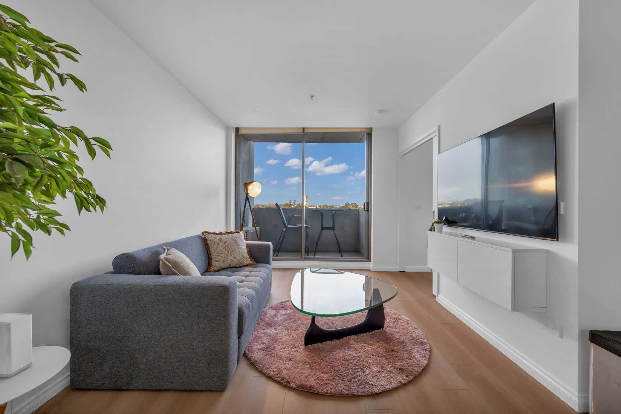 Un salon moderne avec un canapé gris, une table basse en verre et un grand téléviseur fixé au mur.