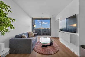 Ein modernes Wohnzimmer mit grauem Sofa, einem Glastisch und einem großen Fernseher an der Wand.
