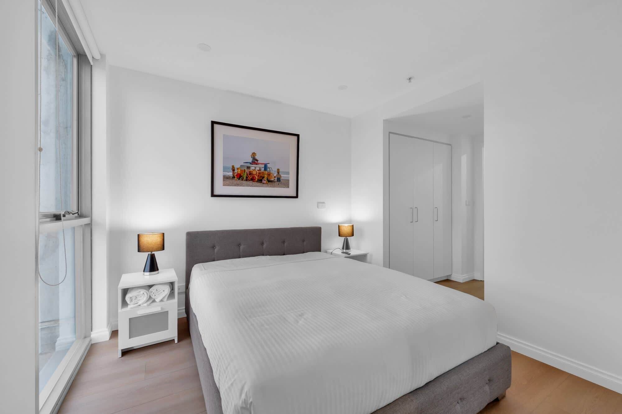 Een slaapkamer met een groot bed, twee nachtkastjes met lampen, een kledingkast, en een ingelijste foto aan de muur.