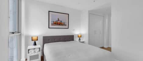 A bedroom with a large bed, two bedside tables with lamps, a wardrobe, and a framed picture on the wall.