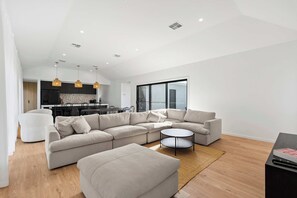 A modern living room with a sectional sofa, a round coffee table, and a dining area in the background.