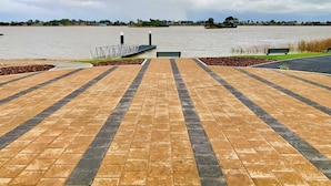 A paved walkway leading to a body of water with a bench and a small island visible in the distance. - Stillwater - holiday home with a private jetty (Wellington East)