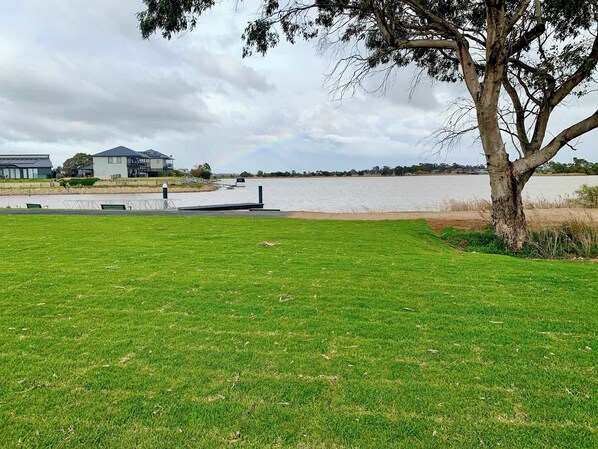 A grassy park area with a body of water, a tree, and a building in the background.