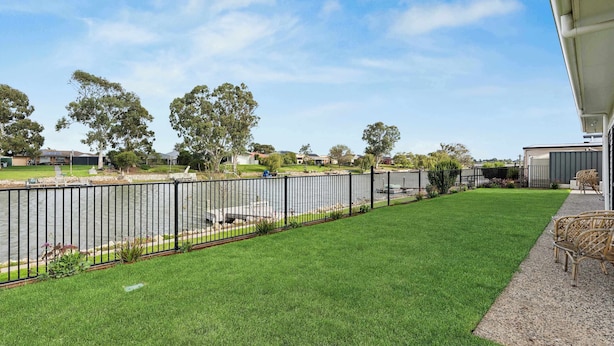 A residential property with a well-maintained lawn, a black metal fence, and a view of a river. - Stillwater - holiday home with a private jetty (Wellington East)