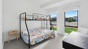 A bunk bed room with a small wooden side table, a large window with a view of the outside, and a carpeted floor. - Stillwater - holiday home with a private jetty (Wellington East)